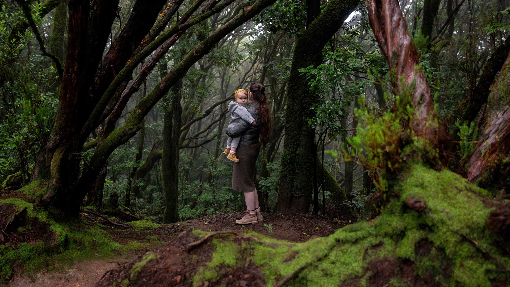 women holding a child standing at the edge of a forest